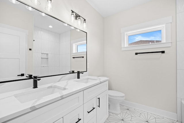 full bath with double vanity, a sink, toilet, and baseboards