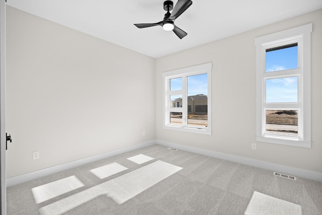 empty room featuring light carpet, ceiling fan, visible vents, and baseboards