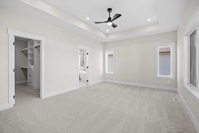 unfurnished bedroom featuring a tray ceiling, a walk in closet, visible vents, carpet flooring, and baseboards