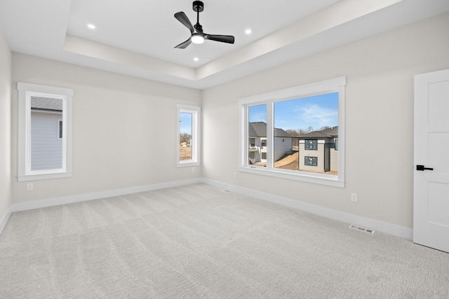 empty room with carpet floors, a tray ceiling, visible vents, and baseboards