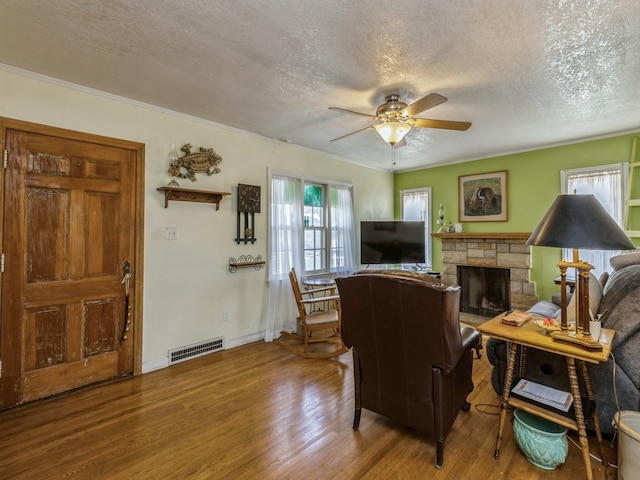 living room featuring ceiling fan, a textured ceiling, a fireplace, crown molding, and hardwood / wood-style floors