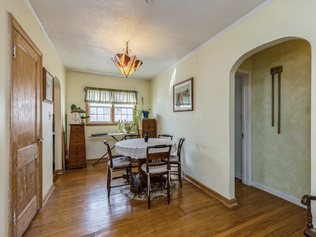 dining space featuring wood-type flooring, a textured ceiling, and crown molding