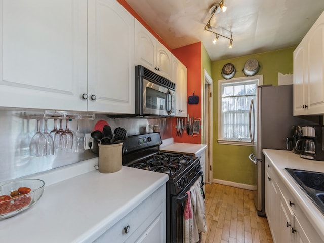 kitchen featuring rail lighting, light hardwood / wood-style floors, white cabinets, black gas stove, and sink