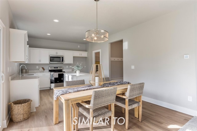 kitchen with white cabinets, sink, decorative light fixtures, light hardwood / wood-style floors, and stainless steel appliances