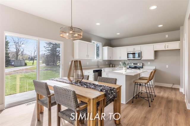 kitchen with white cabinetry, a center island, sink, stainless steel appliances, and decorative light fixtures