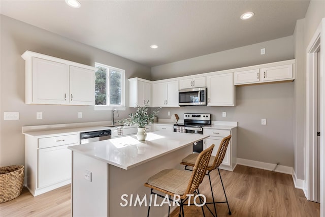 kitchen featuring a kitchen island, light hardwood / wood-style floors, a breakfast bar area, white cabinets, and appliances with stainless steel finishes