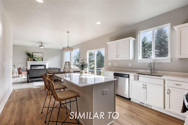 kitchen featuring sink, hanging light fixtures, stainless steel dishwasher, a kitchen island, and white cabinetry