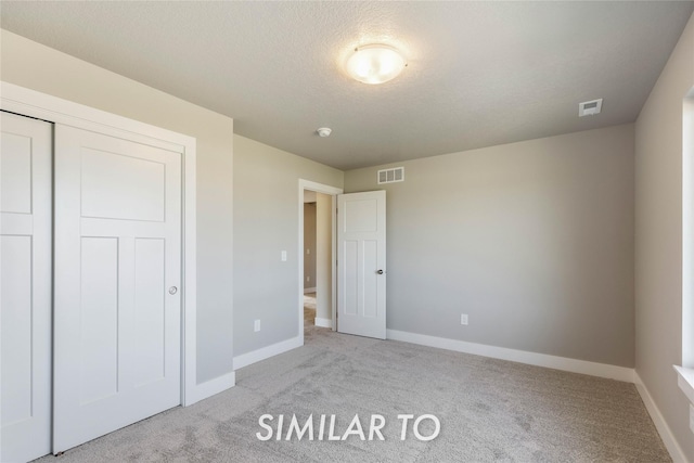 unfurnished bedroom with light colored carpet, a textured ceiling, and a closet