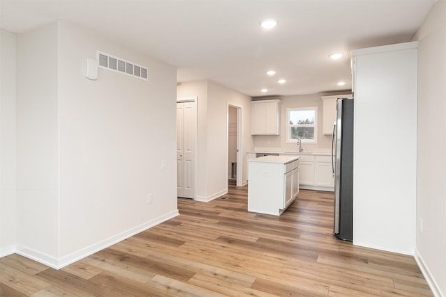 kitchen with stainless steel fridge, light wood-type flooring, a kitchen island, sink, and white cabinetry