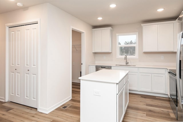 kitchen featuring white cabinetry, a center island, dishwasher, sink, and light wood-type flooring