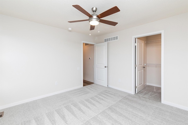 unfurnished bedroom featuring ceiling fan, light colored carpet, a walk in closet, and a closet