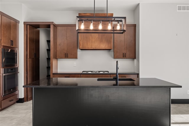 kitchen featuring dark stone countertops, pendant lighting, stainless steel appliances, a center island with sink, and sink