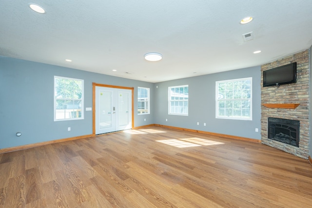 unfurnished living room with a stone fireplace, a textured ceiling, plenty of natural light, and light hardwood / wood-style floors