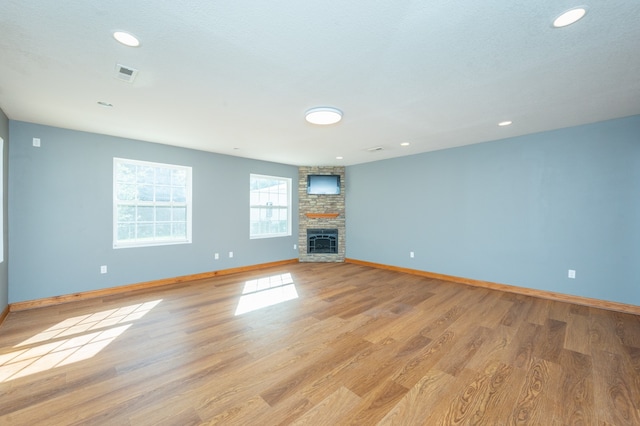 unfurnished living room with a stone fireplace, a textured ceiling, and light wood-type flooring