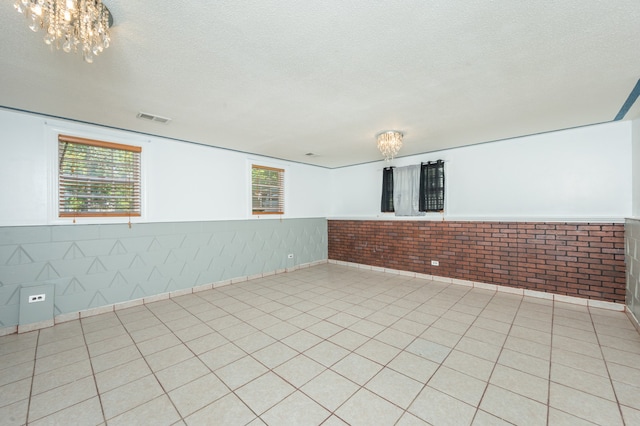 unfurnished room featuring a chandelier, a textured ceiling, brick wall, and light tile patterned flooring