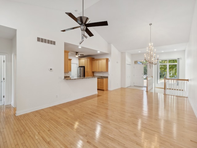 unfurnished living room with high vaulted ceiling, light hardwood / wood-style flooring, and ceiling fan with notable chandelier