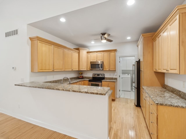 kitchen featuring washer / dryer, light hardwood / wood-style flooring, kitchen peninsula, appliances with stainless steel finishes, and light stone counters