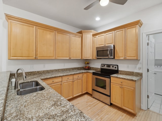 kitchen with light brown cabinets, light wood-type flooring, stainless steel appliances, sink, and light stone counters