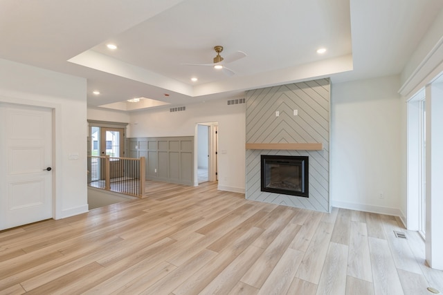 unfurnished living room featuring a large fireplace, ceiling fan, light hardwood / wood-style floors, and a raised ceiling