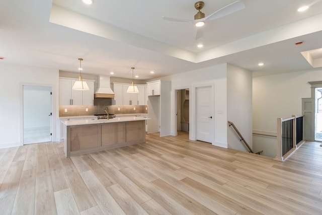 kitchen featuring tasteful backsplash, light hardwood / wood-style flooring, premium range hood, an island with sink, and white cabinets