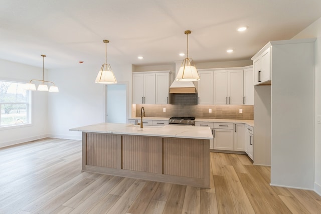 kitchen with sink, white cabinetry, a kitchen island with sink, and stainless steel stove