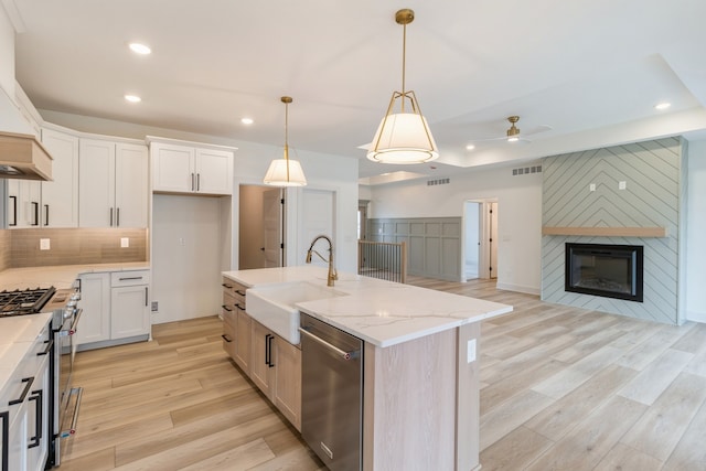 kitchen featuring appliances with stainless steel finishes, light wood-type flooring, white cabinetry, hanging light fixtures, and an island with sink