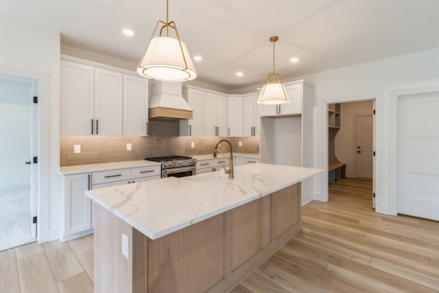 kitchen with white cabinets, high end stove, premium range hood, and a kitchen island with sink