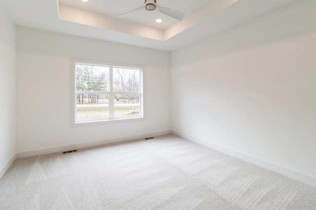 carpeted spare room with a tray ceiling and ceiling fan