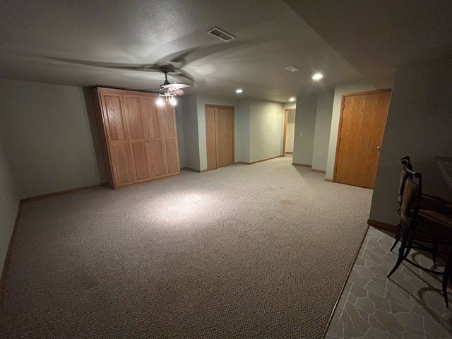 basement with ceiling fan and light carpet