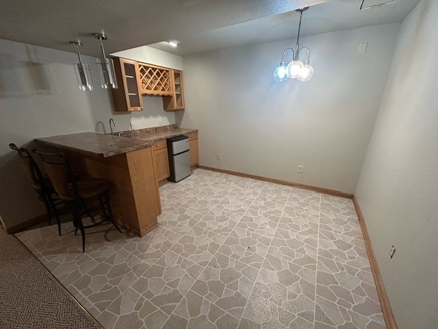 kitchen featuring kitchen peninsula, decorative light fixtures, dishwasher, a kitchen breakfast bar, and a notable chandelier