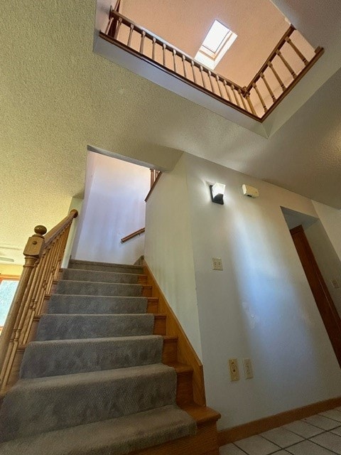 staircase with a high ceiling, tile patterned flooring, a skylight, and a textured ceiling