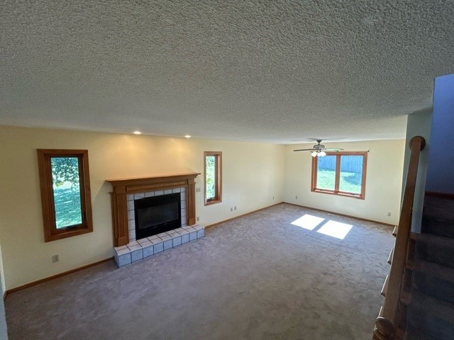 unfurnished living room featuring carpet, ceiling fan, a tile fireplace, and plenty of natural light