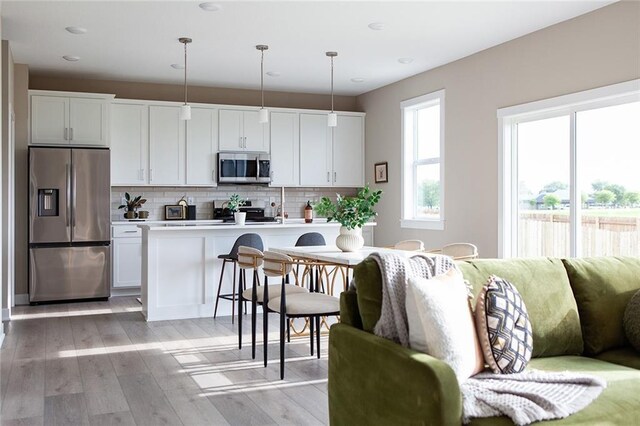 kitchen featuring appliances with stainless steel finishes, light wood-type flooring, tasteful backsplash, decorative light fixtures, and white cabinets