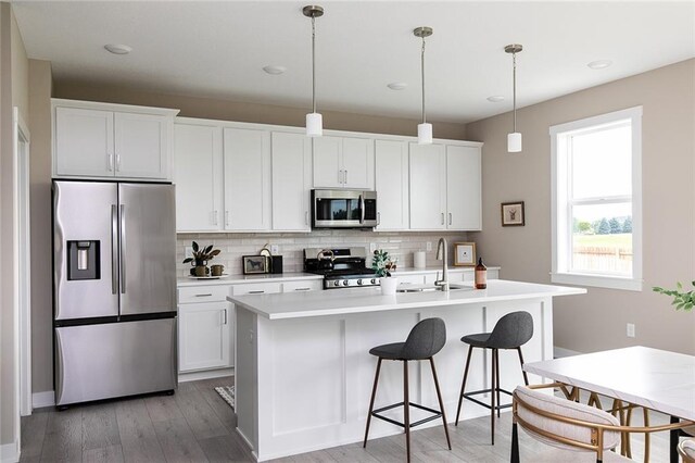 kitchen with appliances with stainless steel finishes, backsplash, white cabinets, hanging light fixtures, and an island with sink