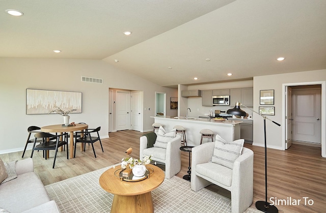 living room with vaulted ceiling, sink, and light hardwood / wood-style flooring