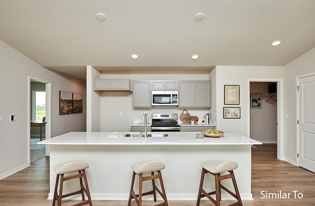 kitchen with sink, stainless steel appliances, an island with sink, and a breakfast bar