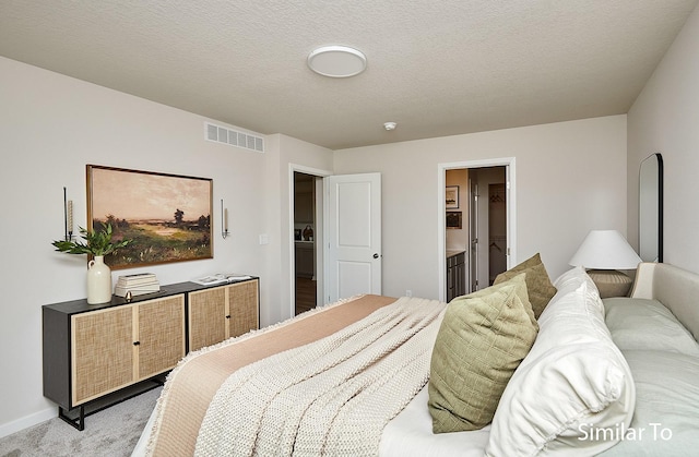 carpeted bedroom featuring a textured ceiling and ensuite bath