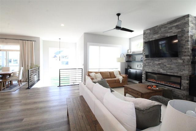 living room with ceiling fan, a stone fireplace, wood-type flooring, and plenty of natural light