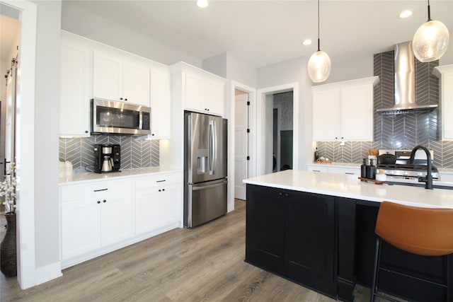 kitchen featuring wall chimney exhaust hood, appliances with stainless steel finishes, decorative light fixtures, and white cabinets