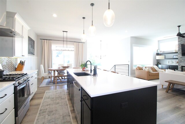 kitchen with sink, hanging light fixtures, stainless steel appliances, wall chimney exhaust hood, and a center island with sink