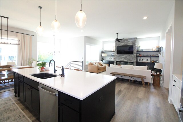 kitchen featuring a stone fireplace, an island with sink, light hardwood / wood-style flooring, sink, and stainless steel dishwasher