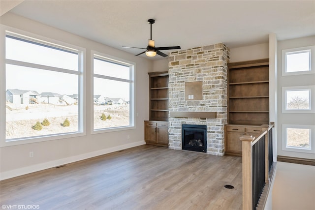 unfurnished living room featuring built in shelves, ceiling fan, light wood-type flooring, and a fireplace