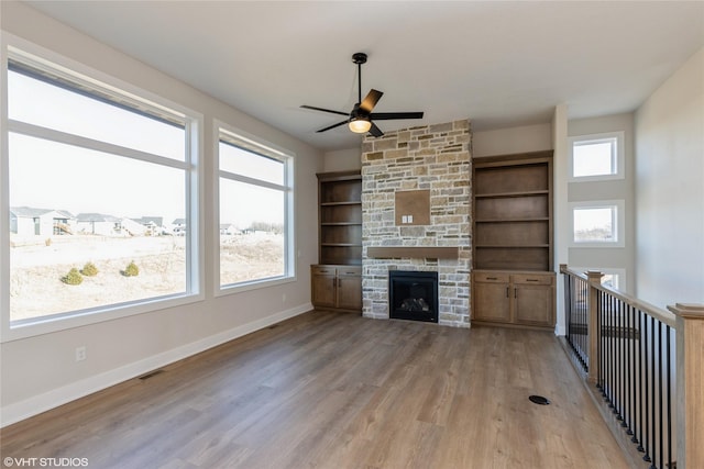 unfurnished living room featuring ceiling fan, built in features, light wood-type flooring, and a fireplace