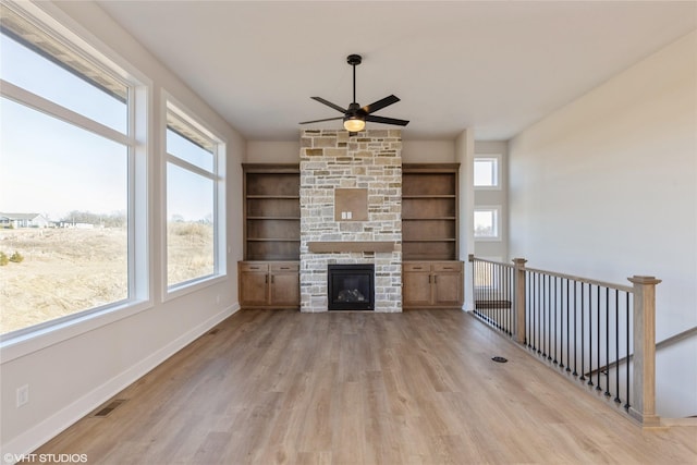 unfurnished living room featuring a stone fireplace, ceiling fan, and light hardwood / wood-style flooring