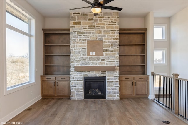 unfurnished living room featuring a stone fireplace, ceiling fan, light hardwood / wood-style flooring, and built in shelves