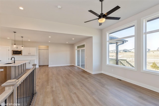 unfurnished living room with ceiling fan, sink, and light hardwood / wood-style flooring