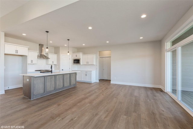 kitchen with white cabinetry, a center island with sink, wall chimney exhaust hood, and pendant lighting