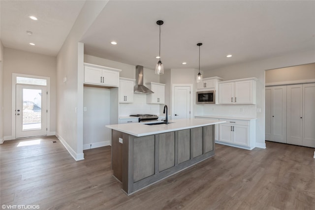 kitchen featuring white cabinetry, built in microwave, sink, wall chimney exhaust hood, and a center island with sink