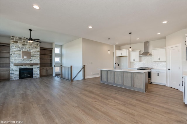 kitchen with pendant lighting, a center island with sink, white cabinets, wall chimney range hood, and stainless steel stove