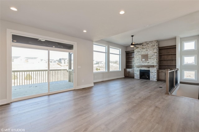 unfurnished living room featuring a stone fireplace, ceiling fan, built in features, and light hardwood / wood-style flooring